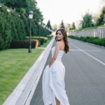 Visão traseira da noiva feliz no vestido de noiva andando na estrada