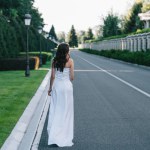 Visão traseira da mulher em vestido de noiva branco andando na estrada