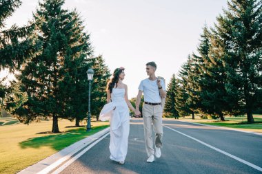 Elele ve birbirlerine birlikte parkta yürürken gülümseyen güzel mutlu genç düğün çifti