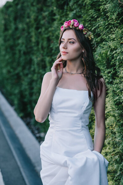 elegant bride posing in traditional white wedding dress and flower wreath