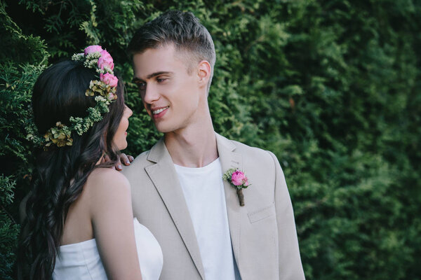 beautiful bride in floral wreath looking at happy groom
