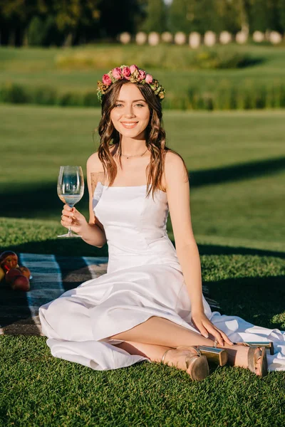 幸せな花嫁の白いドレスでワインのグラスと毛布の上に座って花かざり — ストック写真