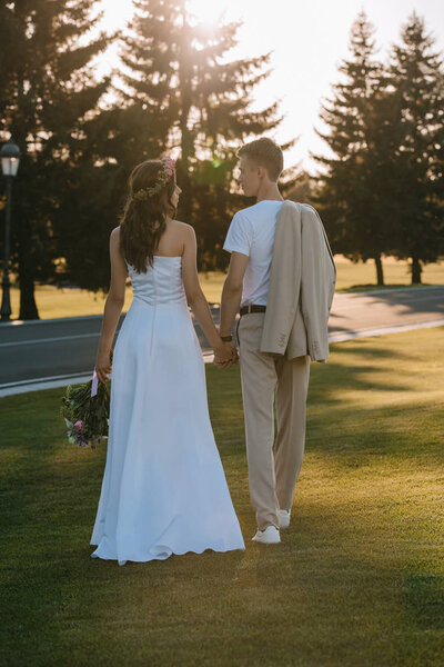 back view of beautiful bride and groom holding hands  