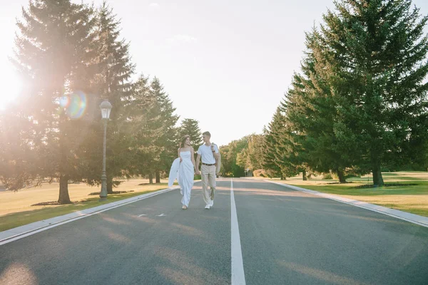 Junges Hochzeitspaar Hält Händchen Und Lächelt Sich Beim Gemeinsamen Spaziergang — kostenloses Stockfoto