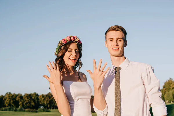 陽気な若いカップルの結婚指輪を示し 美しい公園でカメラに笑顔 — ストック写真