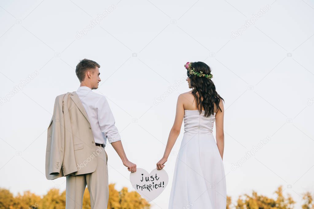 back view of young wedding couple holding heart with just married inscription