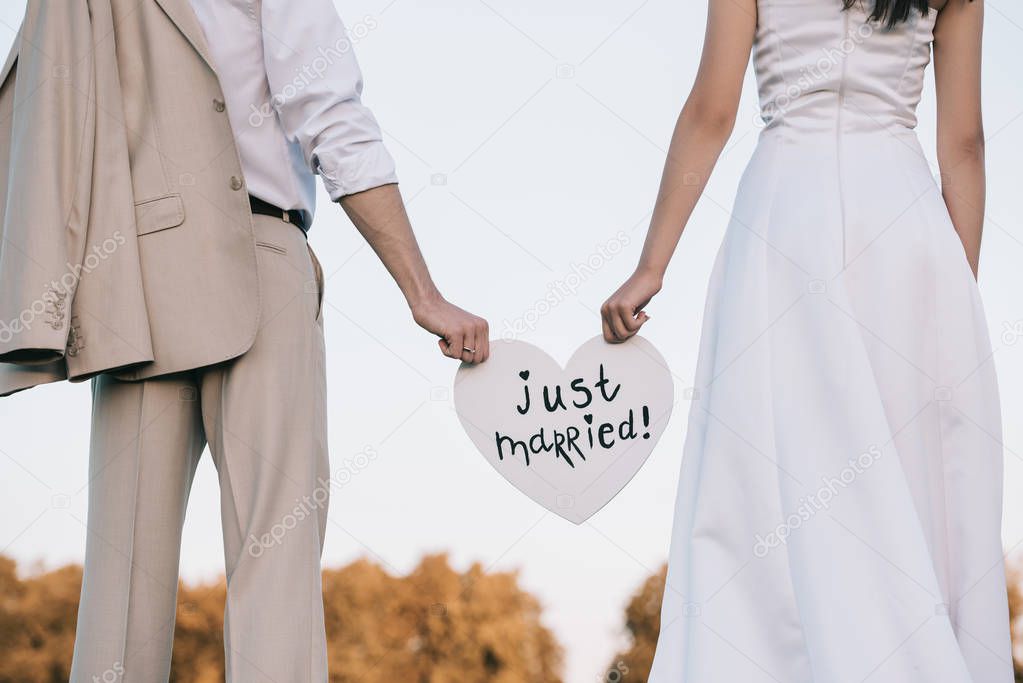cropped shot of young wedding couple holding heart with just married inscription 