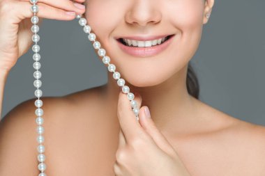 cropped shot of smiling woman with white teeth and pearls in hands isolated on grey clipart