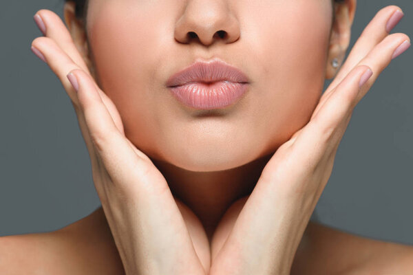 partial view of woman with hands at cheeks and duck face isolated on grey