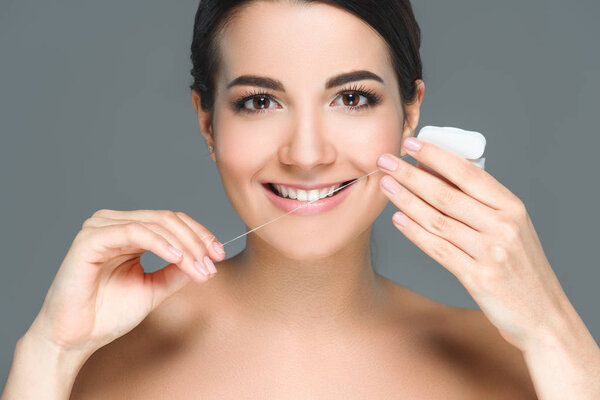 portrait of smiling woman with beautiful white teeth and dental floss isolated on grey