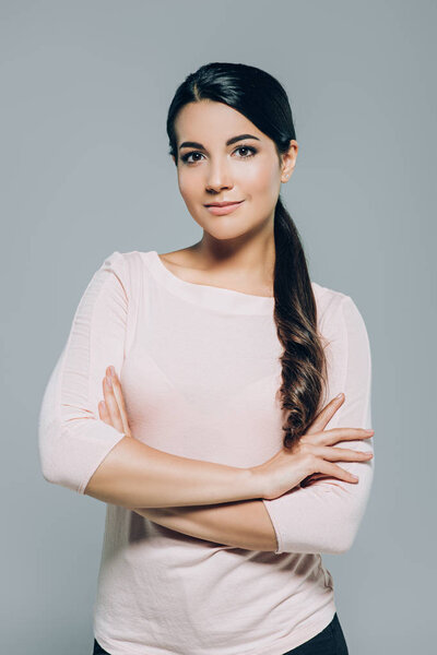Портрет привлекательная брюнетка женщина со скрещенными руками позирует изолированно на сером
