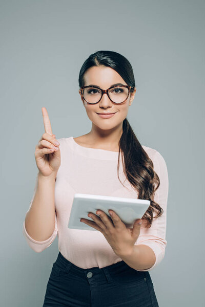 портрет улыбающейся брюнетки в очках с цифровым планшетом, указывающим на серый
