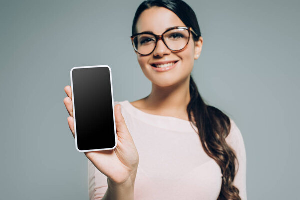 young woman showing smartphone with blank screen, isolated on grey