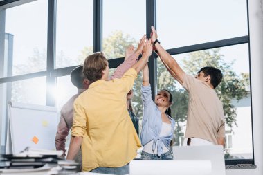 happy businesspeople celebrating success and giving high five in office