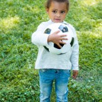 Чарівна афроамериканська дитина тримає футбольний м'яч і дивиться в парку