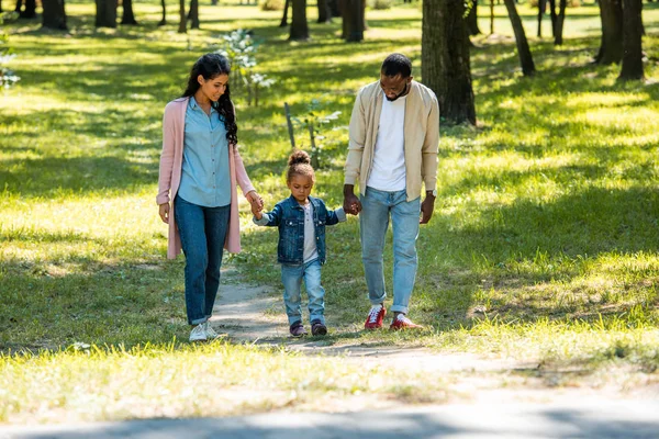 アフリカ系アメリカ人の両親と娘の手を押しながら公園を歩いて — ストック写真