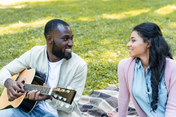 Sonriente Guapo Afroamericano Novio Jugando Guitarra Acústica Para Novia Parque — Foto de stock gratis