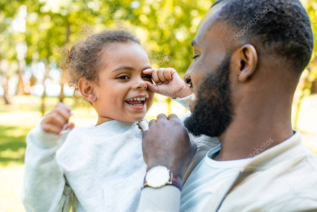 smiling african american father looking at happy daughter in park
