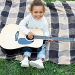Высокий угол обзора улыбающегося очаровательного африканского ребенка с акустической гитарой в парке