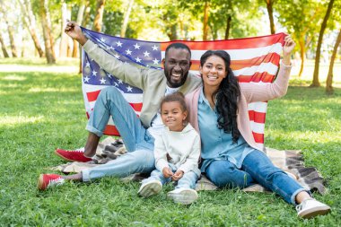 Afrikalı Amerikalı anne ve kızı parkta piknik Amerikan bayrağı tutarak gülümseyen