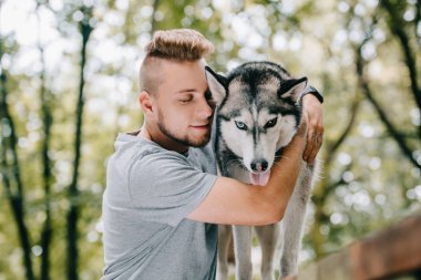 young man hugging husky dog in park clipart