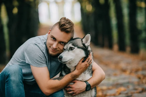 Jovem Sorridente Homem Abraçando Husky Cão Parque — Fotografia de Stock
