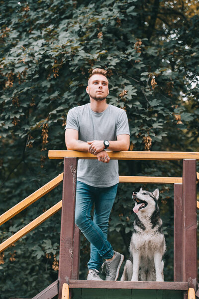handsome man standing on stairs with husky dog 