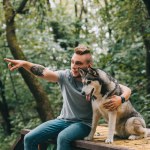 Cynologist i siberian husky pies siedzi w parku, wskazując gdzieś człowieka