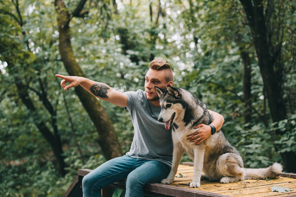 young man and siberian husky dog sitting in park, man pointing somewhere