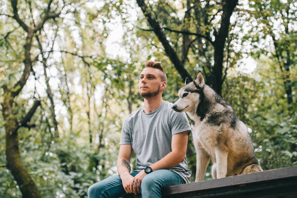 handsome man with siberian husky dog sitting in park