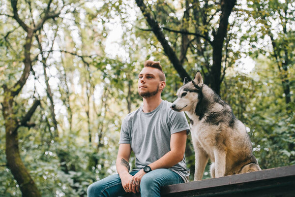 handsome man with siberian husky dog sitting in park