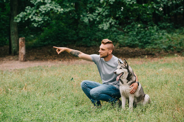 young man showing something to siberian husky dog in park