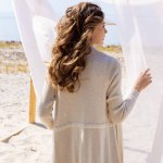 Visão traseira da mulher de pé perto de decoração de madeira com renda cortina branca na praia de areia