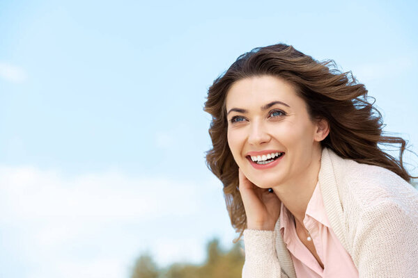 portrait of smiling beautiful woman with blue cloudy sky on background