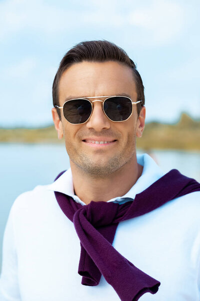 portrait of smiling man in sunglasses looking at camera with river on background