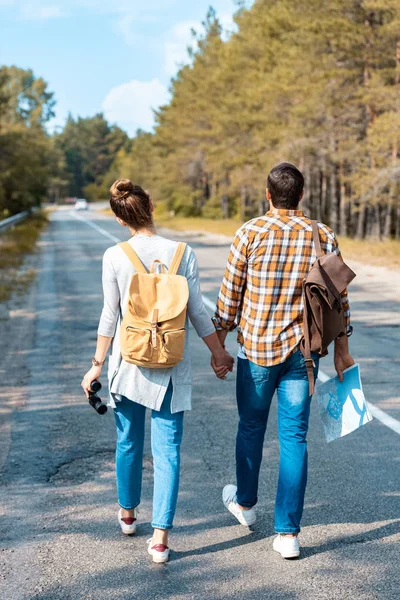 Visão Traseira Turistas Com Mochilas Mãos Dadas Enquanto Caminham Estrada — Fotografia de Stock