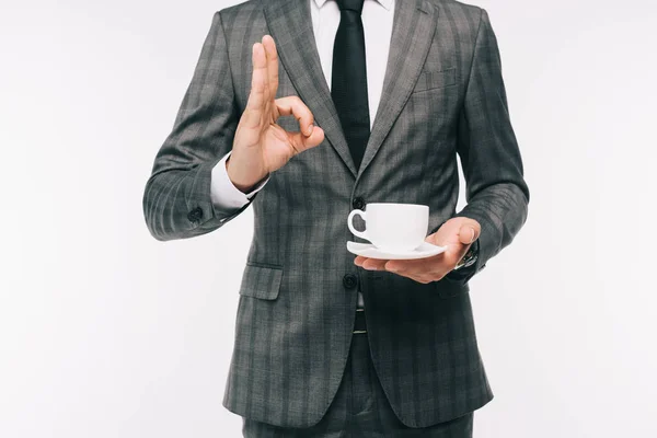 裁剪图像的商人举行杯咖啡 并显示好手势孤立的白色 — 免费的图库照片
