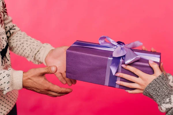 cropped image of girlfriend giving present in violet box to boyfriend isolated on pink