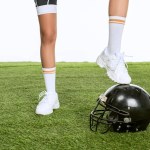 Corte tiro de mulher em pé no capacete de futebol americano na grama verde isolado no branco