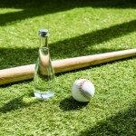 Glass water battle with baseball ball and bat lying on green grass