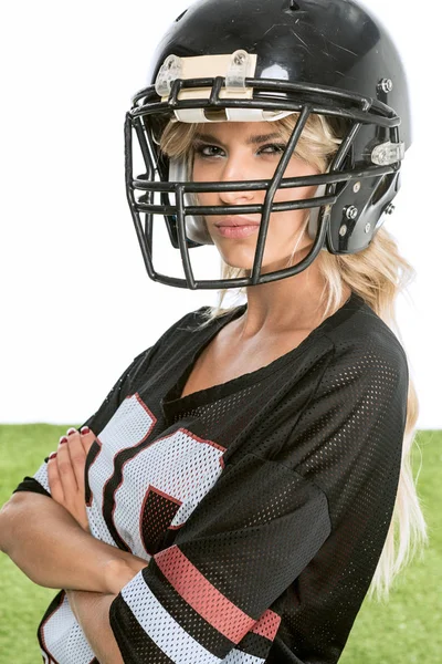 serious young woman in american football uniform looking at camera with crossed arms isolated on white