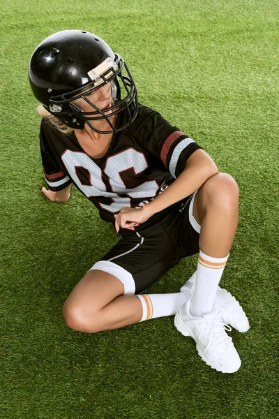 Athletic Młoda Kobieta Mundurze Futbolu Amerykańskiego Siedząc Trawie Szukasz Drogi — Darmowe zdjęcie stockowe