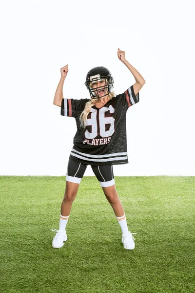 young woman in american football uniform celebrating victory while standing on grass isolated on white