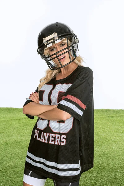 angry young woman in american football uniform looking at camera with crossed arms isolated on white