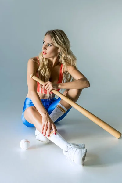 Sportliche Junge Frau Mit Baseballschläger Sitzt Auf Grau Und Schaut — kostenloses Stockfoto