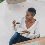 Vista de ángulo alto de la atractiva mujer de negocios afroamericana elegante sosteniendo la taza de café en la oficina