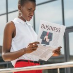 Elegante hermosa mujer de negocios afroamericana leyendo periódico cerca del centro de negocios