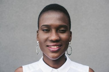gülümseyen şık çekici Afrikalı-Amerikalı kadın kamera gri duvarının yakınında bakarak portresi