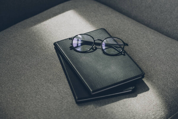eyeglasses and two notebooks on grey armchair in office