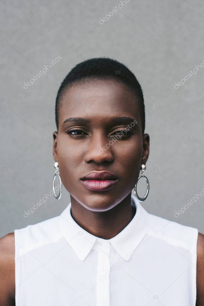 portrait of fashionable attractive african american woman looking at camera near grey wall